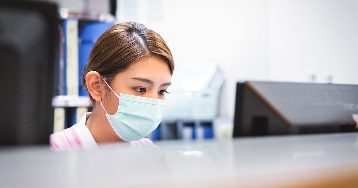 A nurse wearing a surgical mask working at reception
