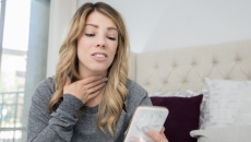 
  Person on a cellphone holding their throat
