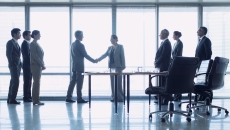 Two people shaking hands with six others watching
