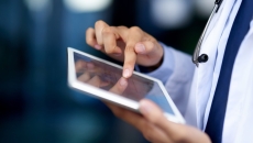 Healthcare provider holding a tablet while wearing a lab coat and stethoscope