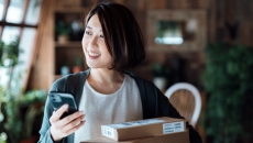 Person standing in a house holding a phone with a box in front of them