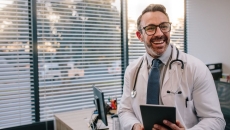 Healthcare provider sitting on a desk holding a tablet while smiling