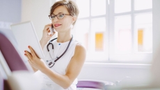 Healthcare provider looking at a tablet while wearing a white shirt and a stethoscope around their neck