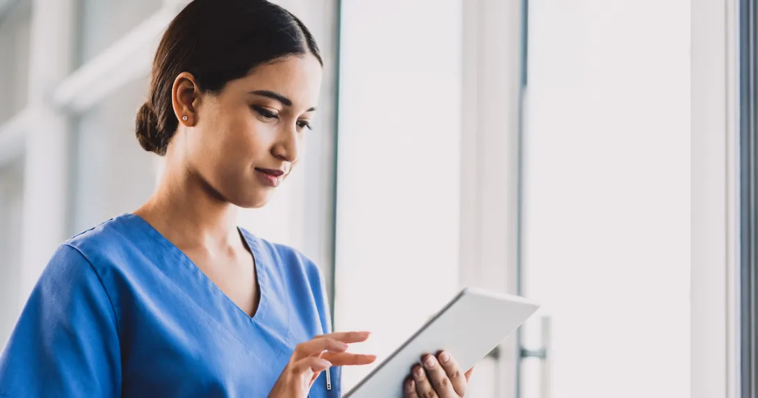 Nurse standing in a hallway holding a tablet Nurse standing in a hallway holding a tablet