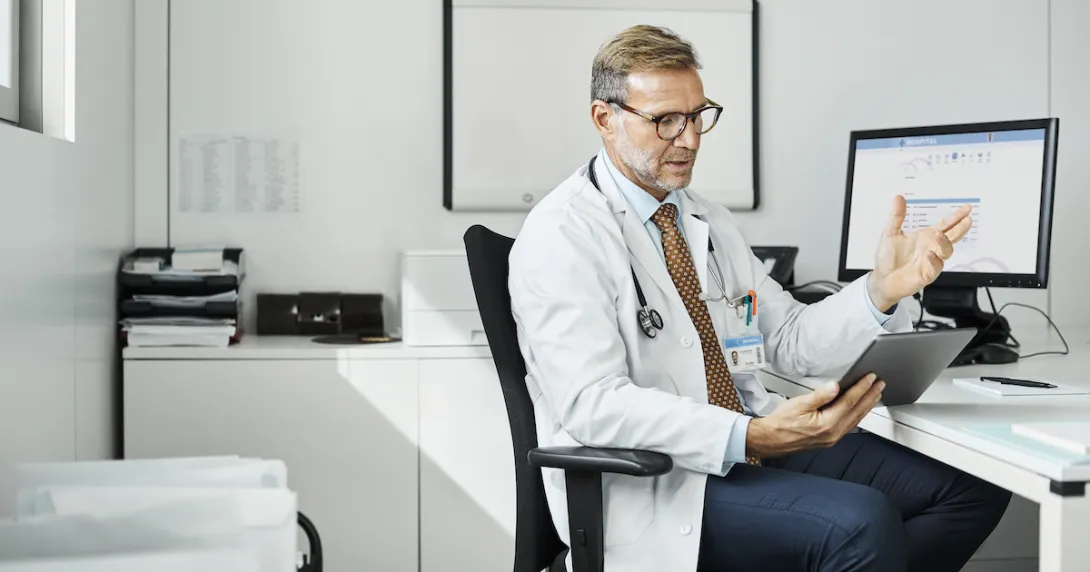 Doctor sitting in a chair at a desk while looking at a tablet