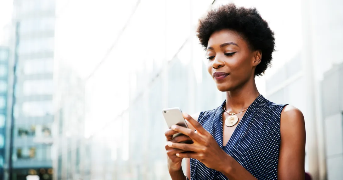 Person standing on the street while looking at their phone with a blurred city background