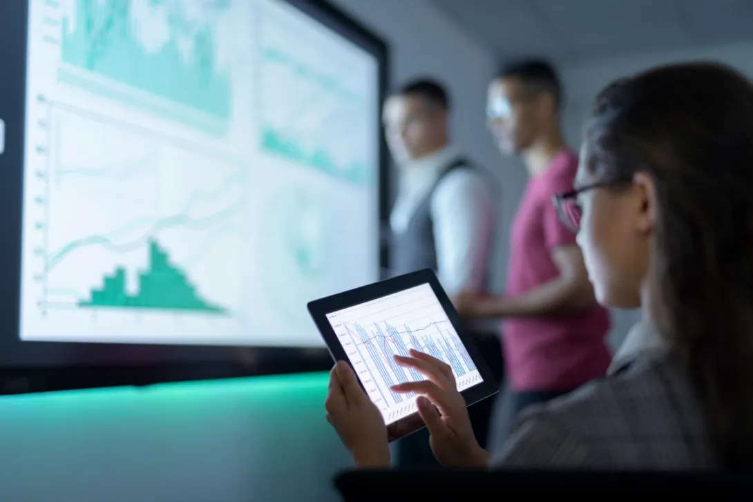 Person holds tablet while looking at information on a large screen