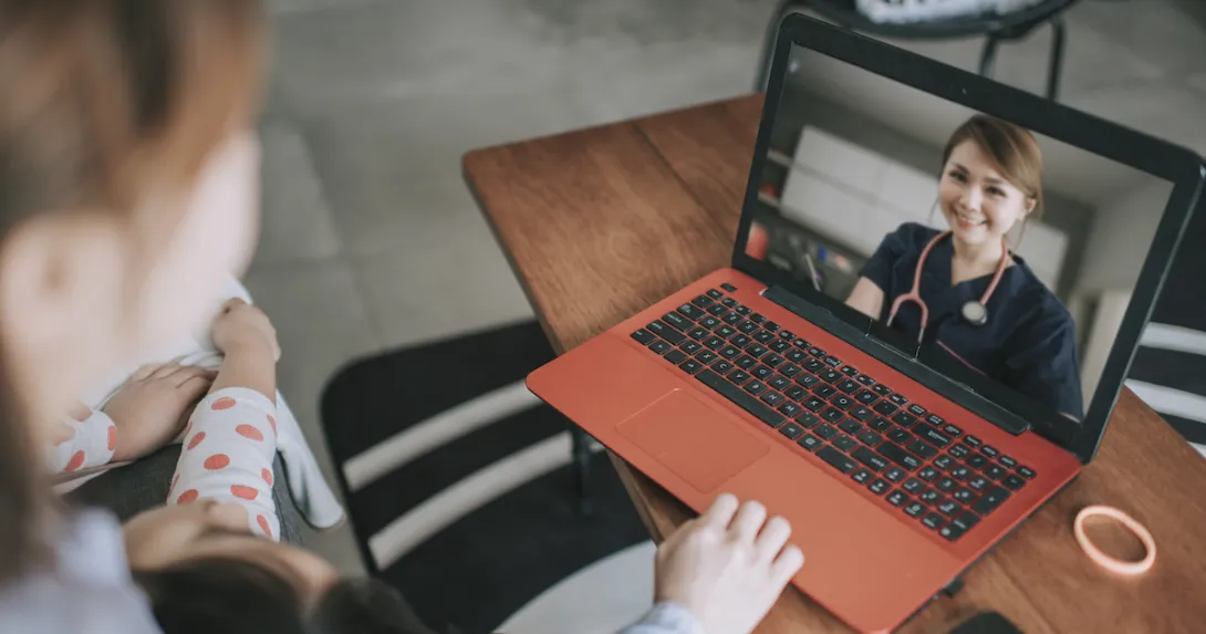 Two people sitting on a couch while looking at a computer with a healthcare provider on the screen