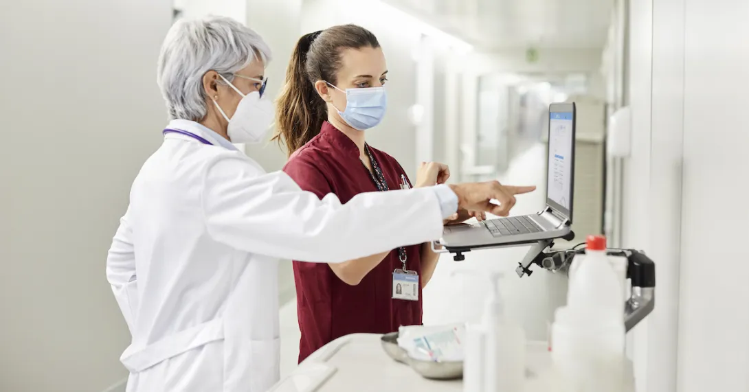 
  A doctor and a nurse using a laptop in a hospital.
