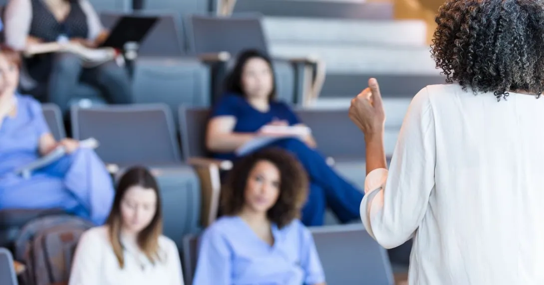 
  Several people sitting in a classroom with a teacher with their back faced to the camera
