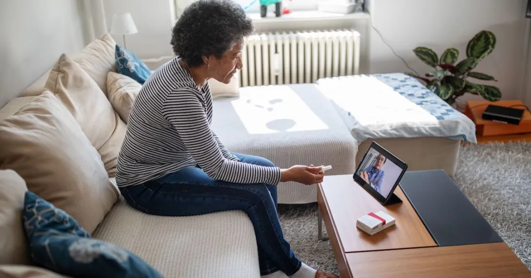 
  Person sitting on their couch speaking to a healthcare provider on a tablet
