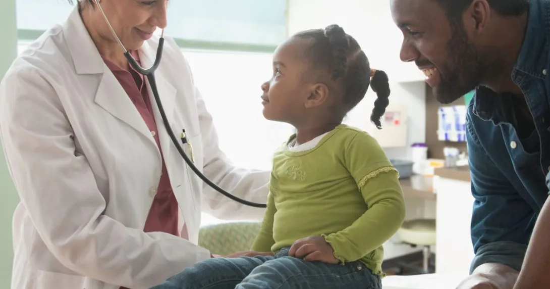 
  Healthcare provider and another adult standing by a child on an exam table
