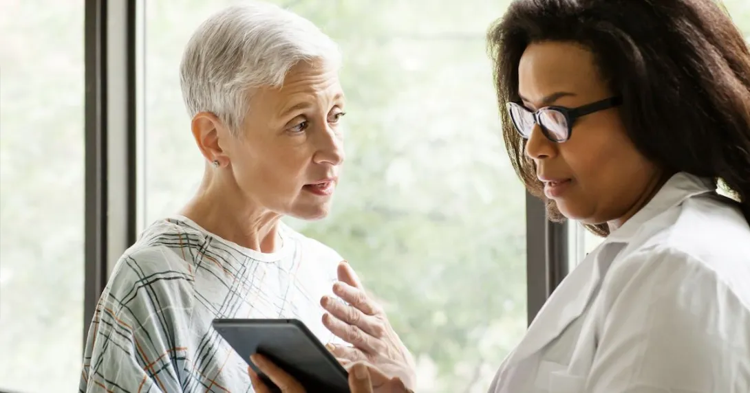 
  Healthcare provider talking to a patient in a hospital gown while both look at a tablet
