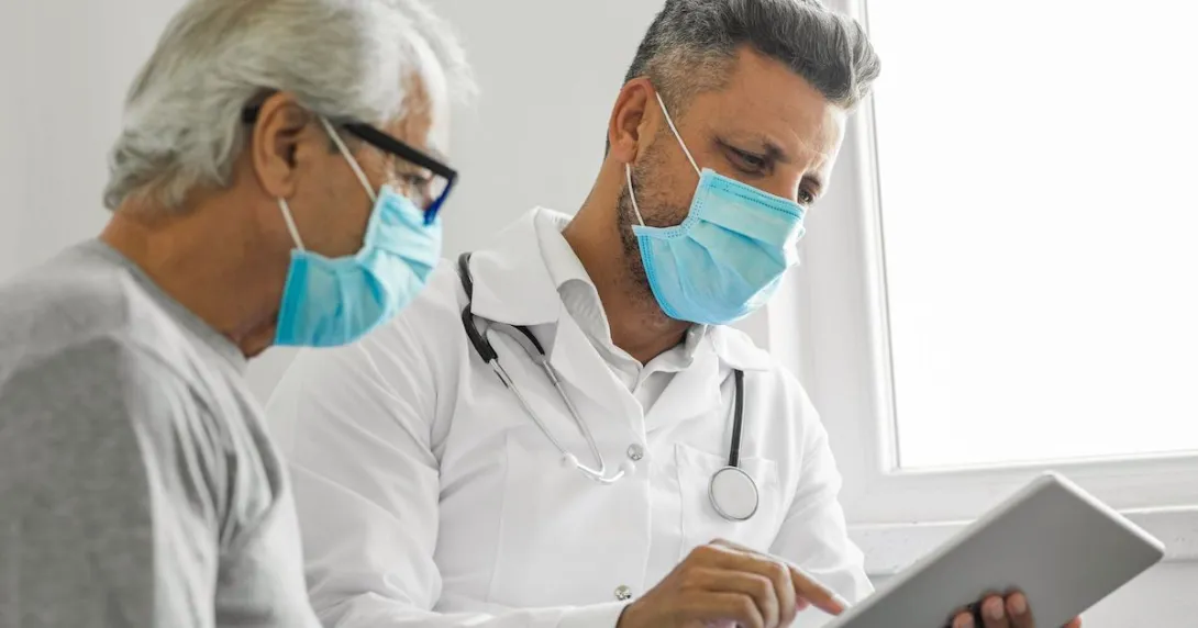 
  Healthcare provider and patient sitting next to each other wearing masks and looking at a tablet
