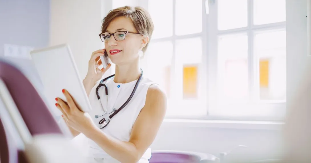 A doctor reading a patient's chart while discussing it with another doctor on the phone