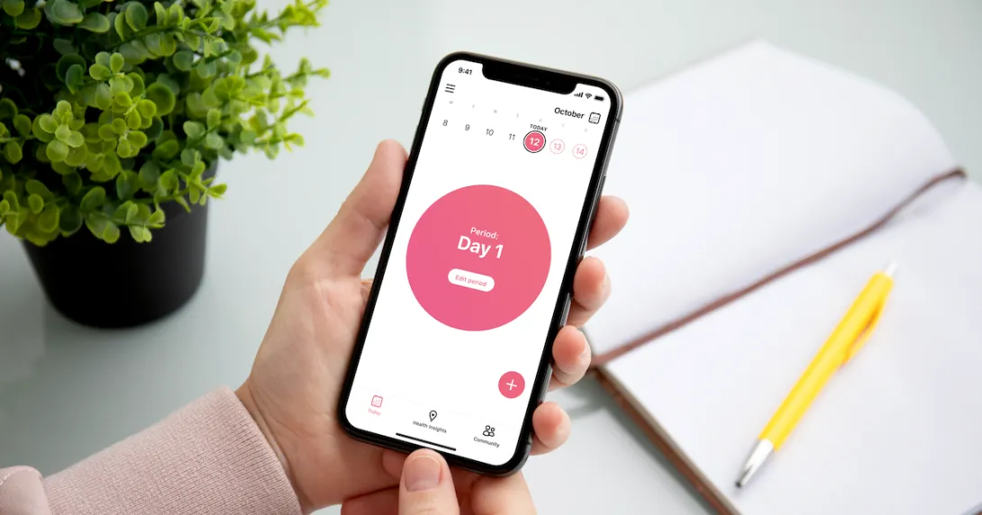 A person holding a smartphone displaying the app. The screen reads, "Period: Day 1."