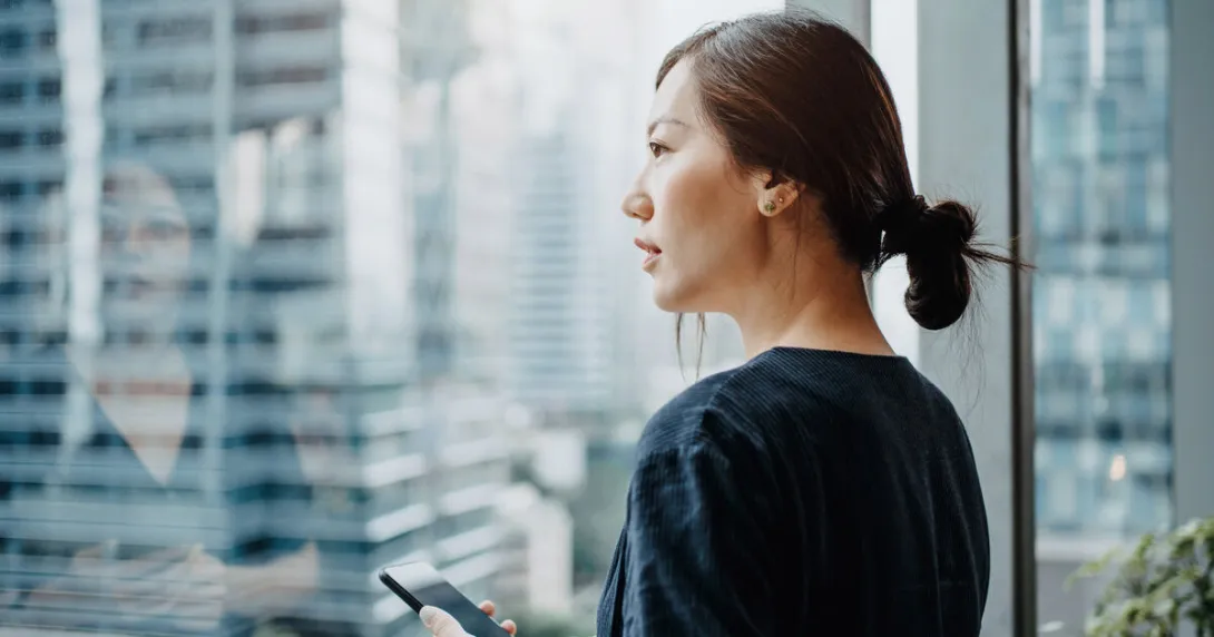 A person holding a phone looking out the window A person holding a phone looking out the window