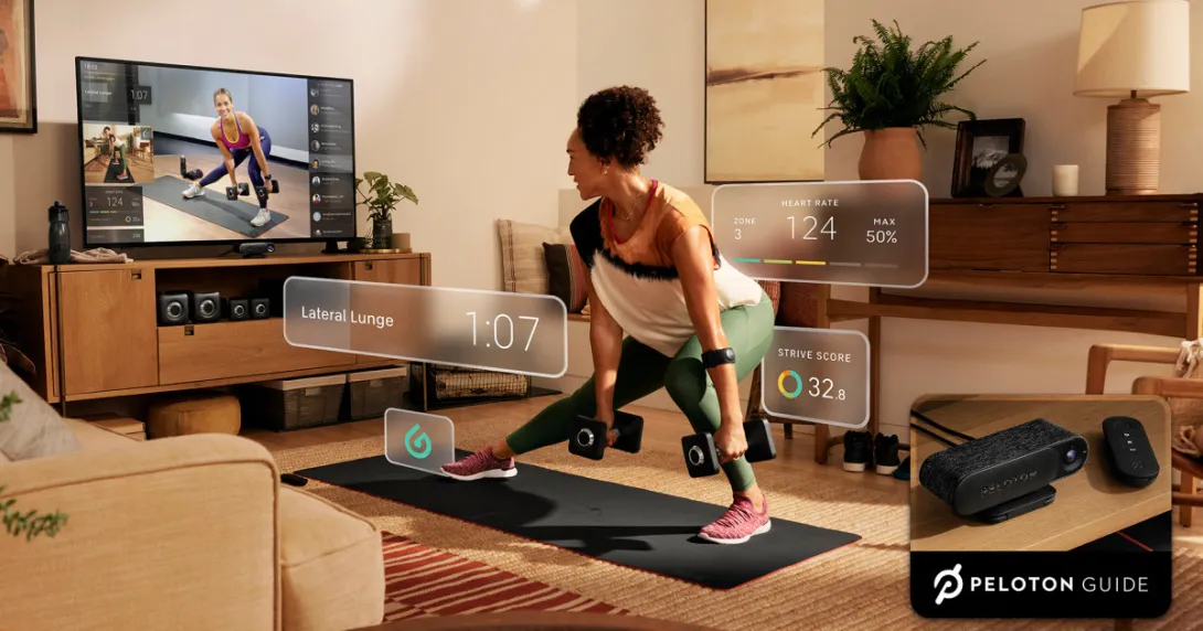 A woman lifting weights using the Peloton Guide while watching an instructor on her TV