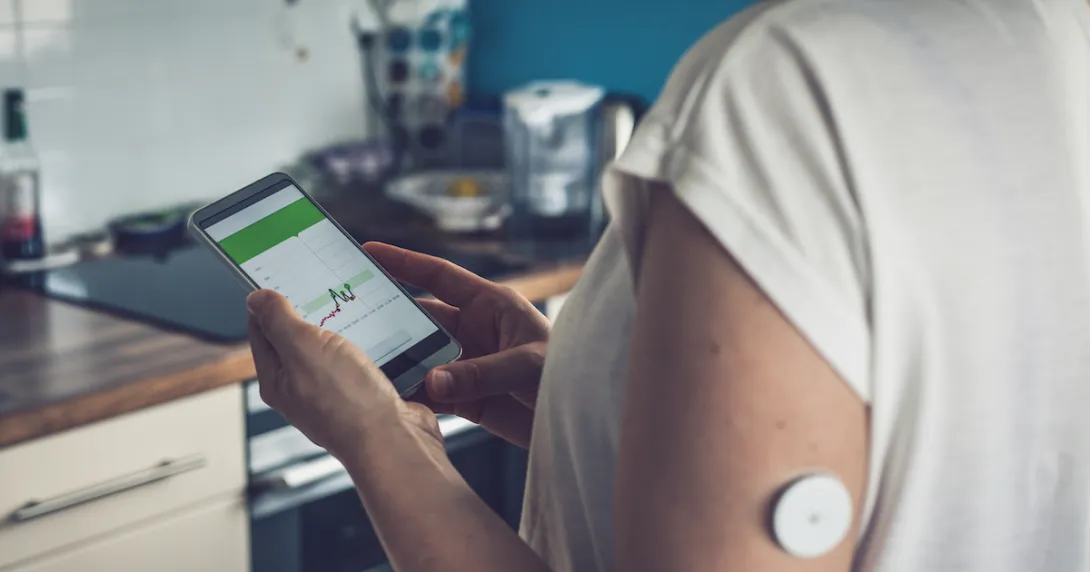 Woman checking glucose level with a remote sensor and mobile phone