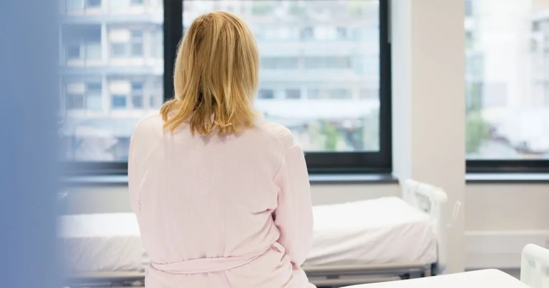 A person sitting on a hospital bed with her back to the camera.