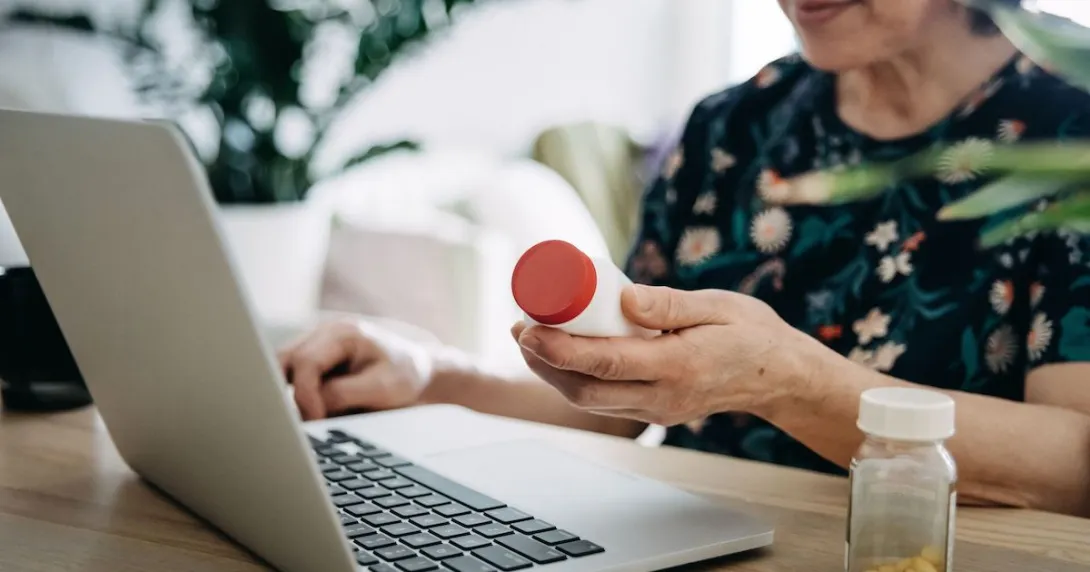 A close up of a person holding a pill bottle while using a laptop